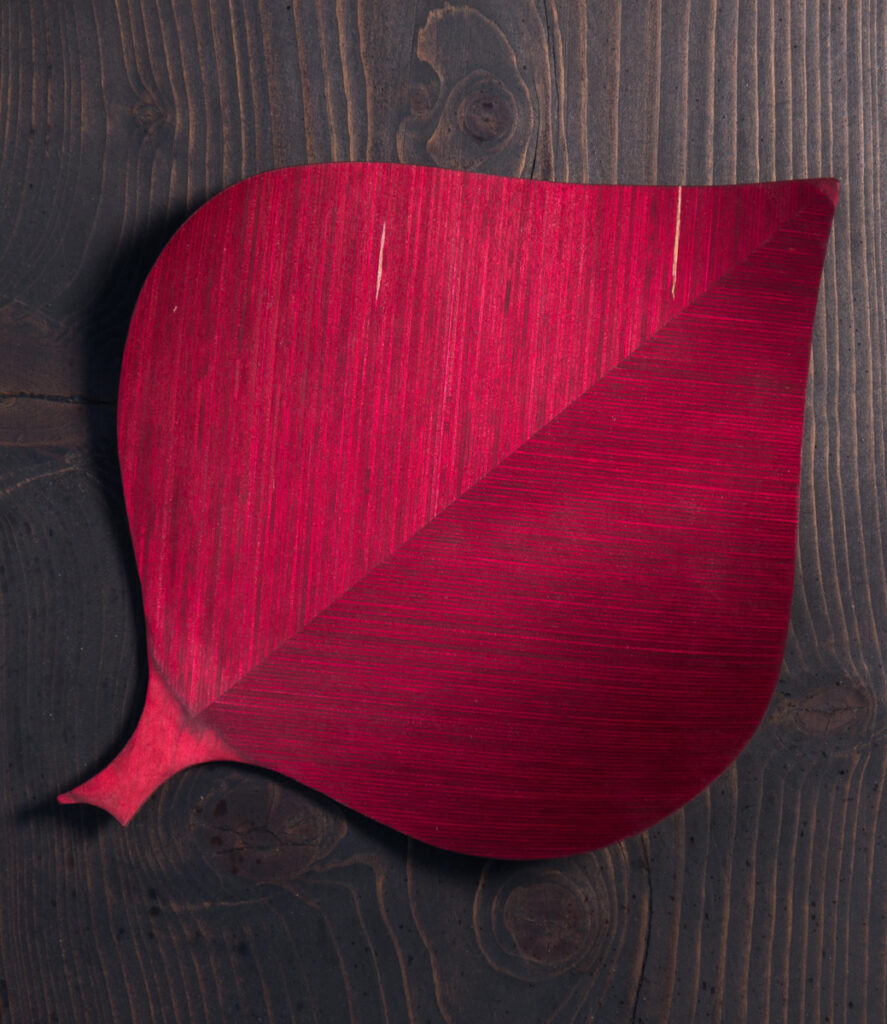 Punainen lehden muotoinen puulautanen puisella pöydällä.