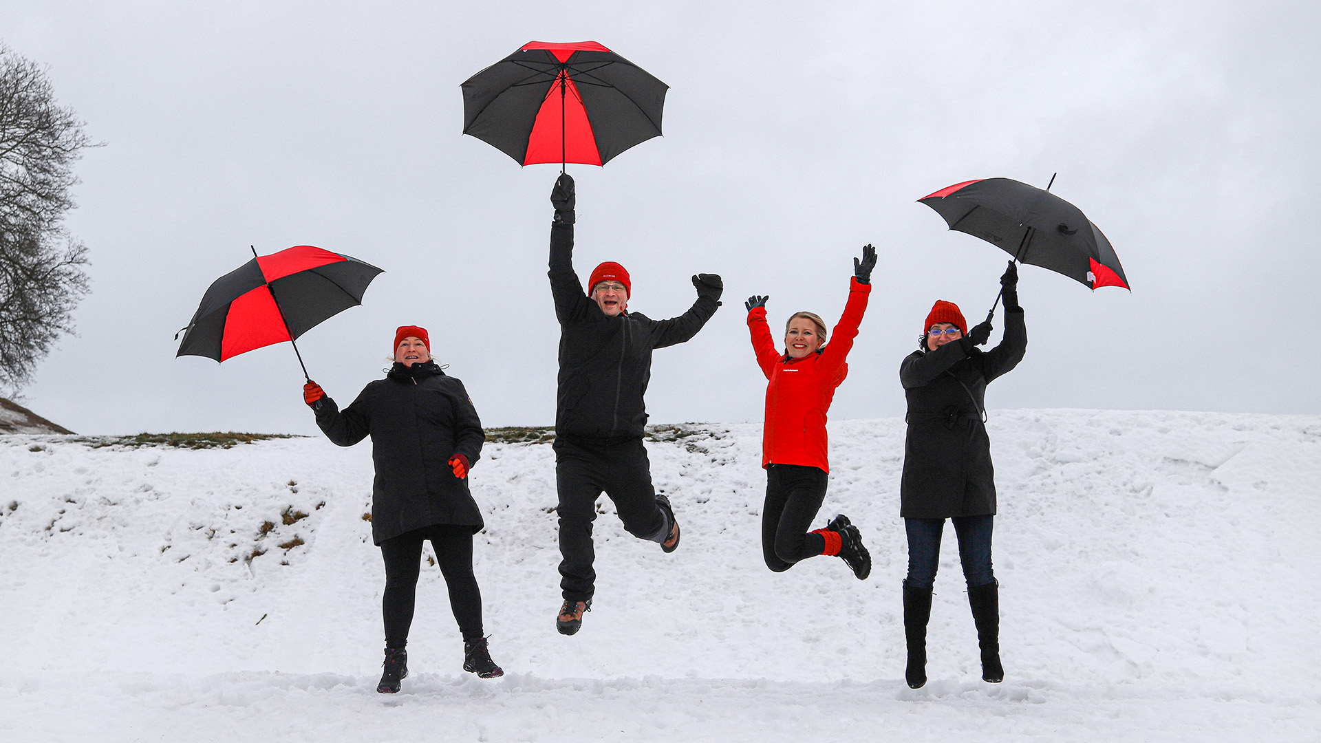 Etelä-Karjalan liiton henkilöstöä sateenvarjojen kanssa hyppäämässä ilmaan lumisessa talvimaisemassa.
