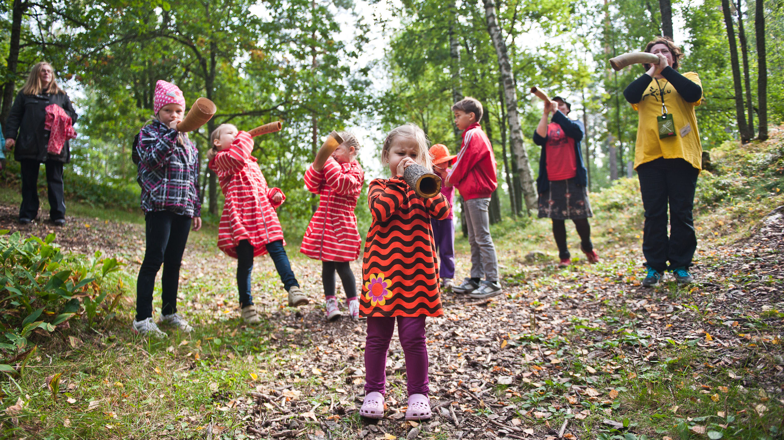 Metsässä lapsia, jotka puhaltavat torveen.