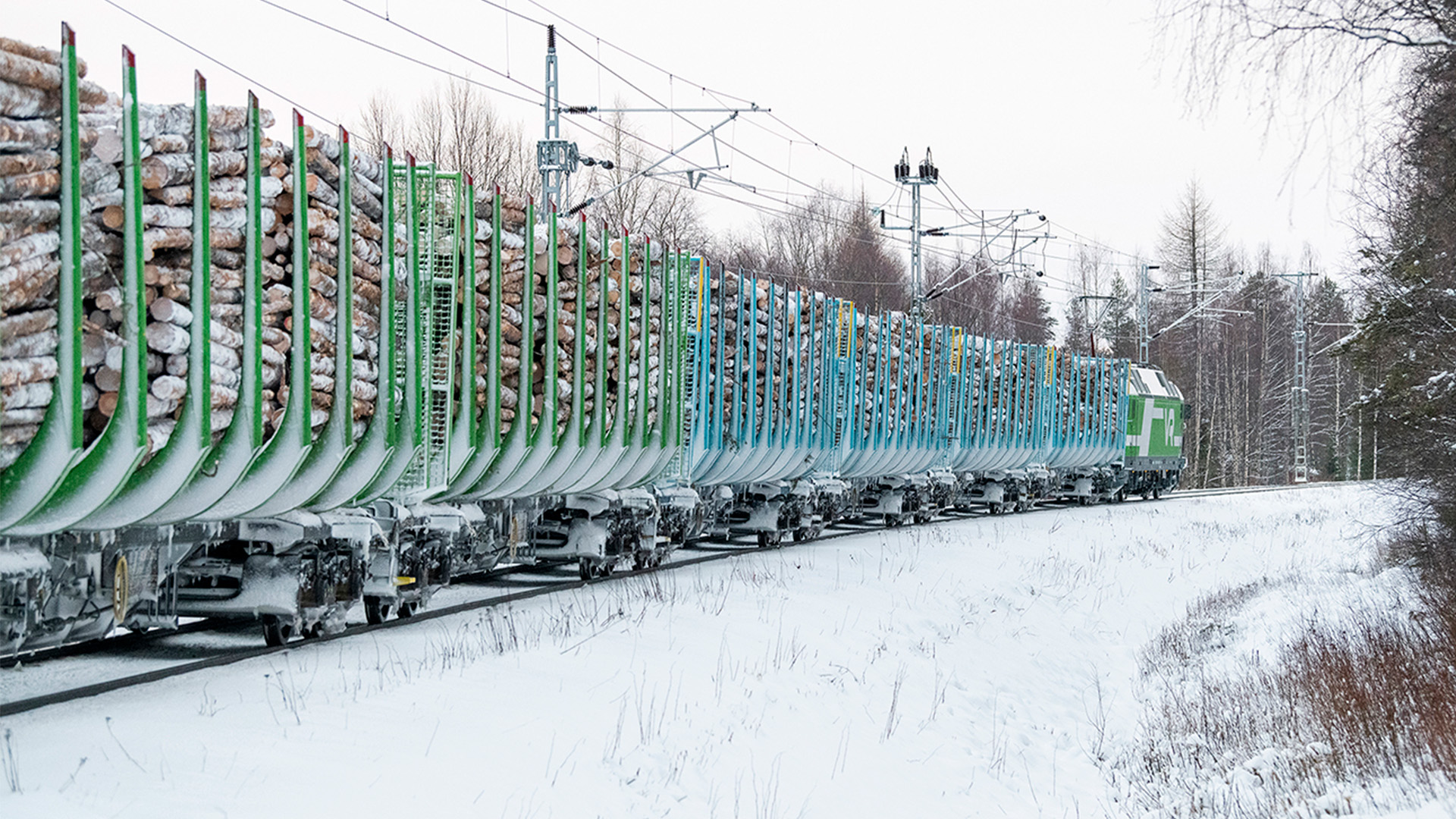 Raakapuuta kuljettava juna kulkee lumisessa maisemassa.