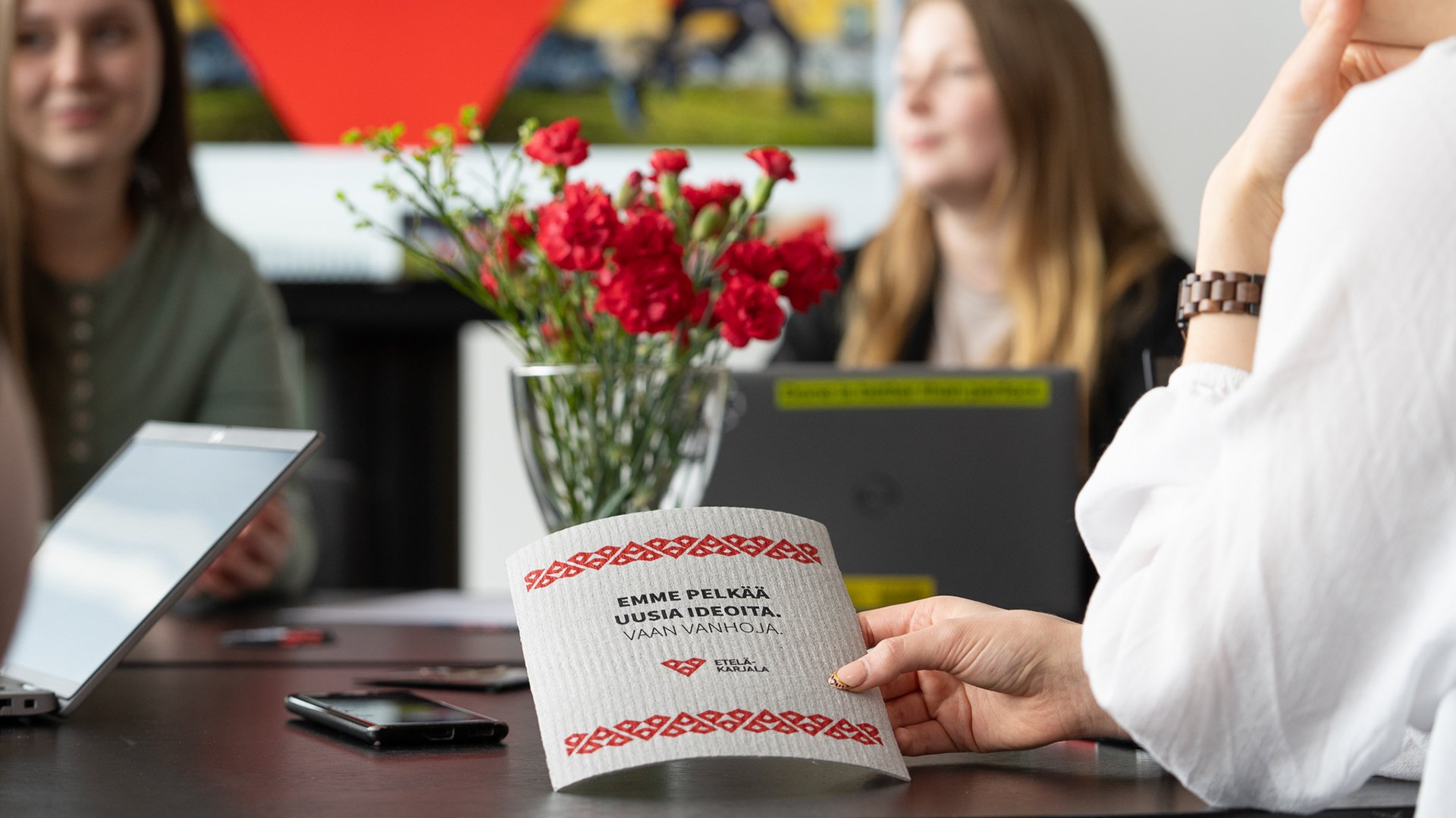 Ihmisiä neuvottelutilassa, etualalla on tiskirätti, jossa Etelä-Karjalan logo sekä teksti "Emme pelkää uusia ideoita vaan vanhoja".