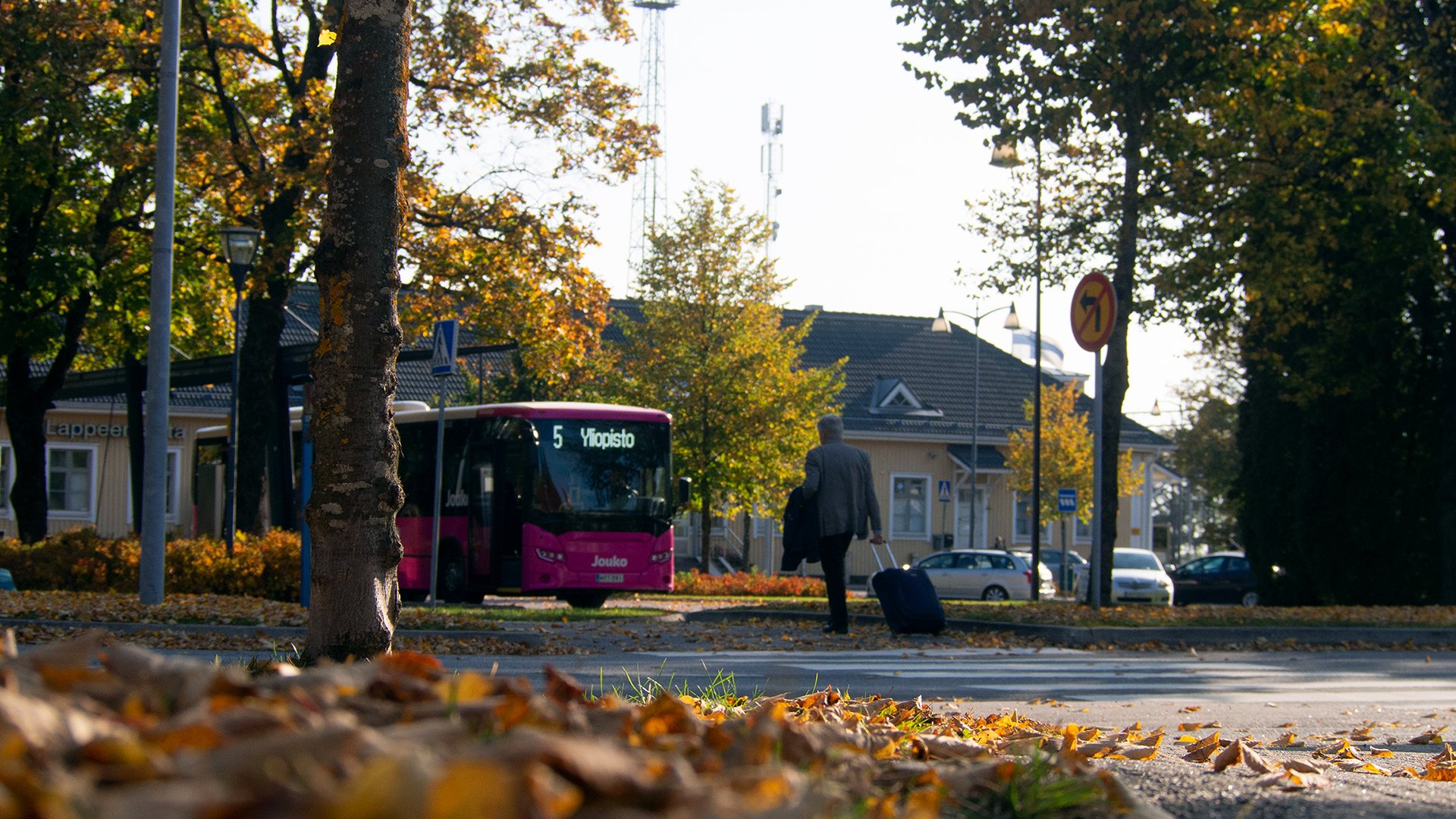 Mies kävelee matkalaukun kanssa Lappeenrannan rautatie-asemalla. Taustalla näkyy linja-auto sekä asemarakennus.